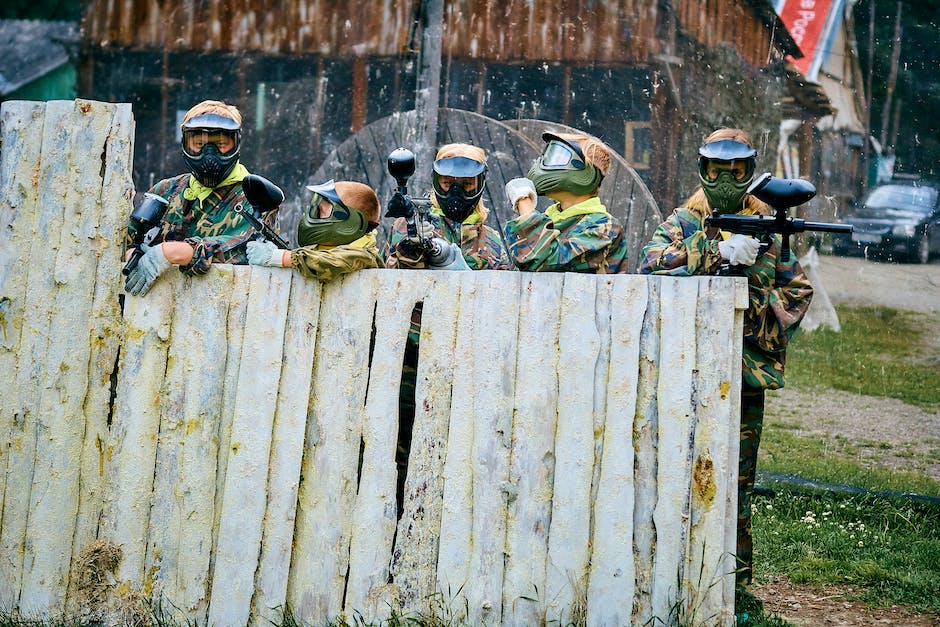 A scenic field with players in paintball gear taking cover behind obstacles and trees.